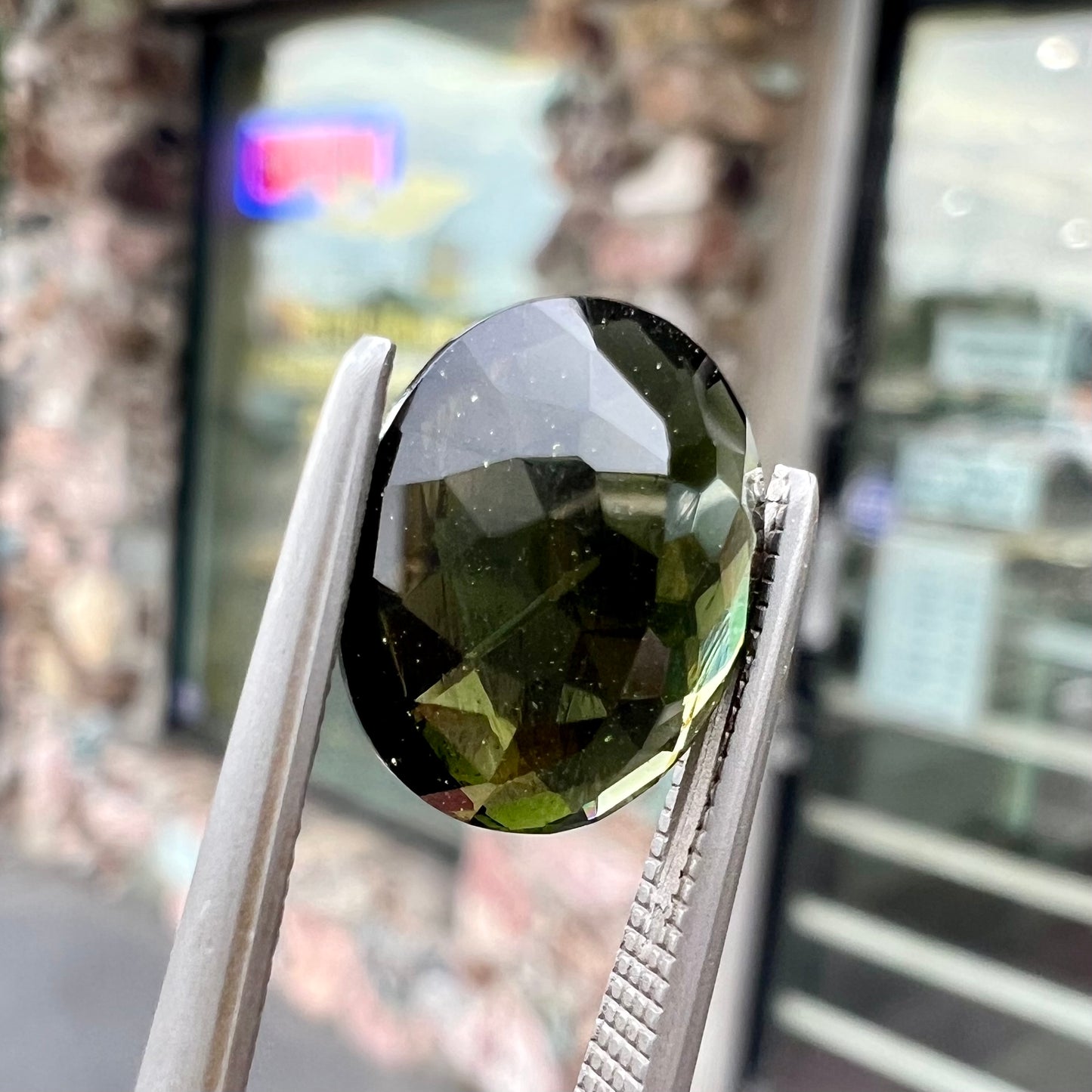 A loose, oval checkerboard cut natural moldavite gemstone.  The stone is dark green color.