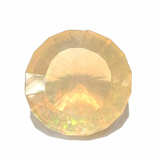 A loose, round faceted Mexican fire opal gemstone.  The stone is transluscent light orange color with rainbow play of color in the sunlight.