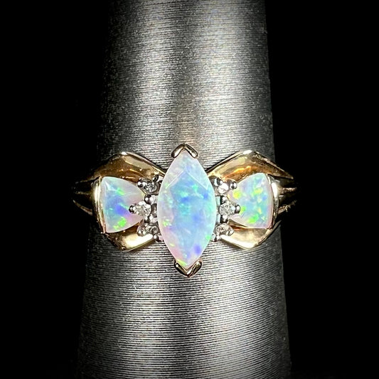 A yellow gold, diamond accented ring set with a marquise cut and two trillion cut lab created opals.