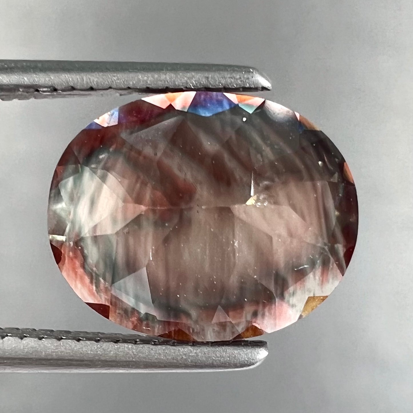 A loose, oval cut oregon sunstone.  The gem is reddish orange with a green secondary color.