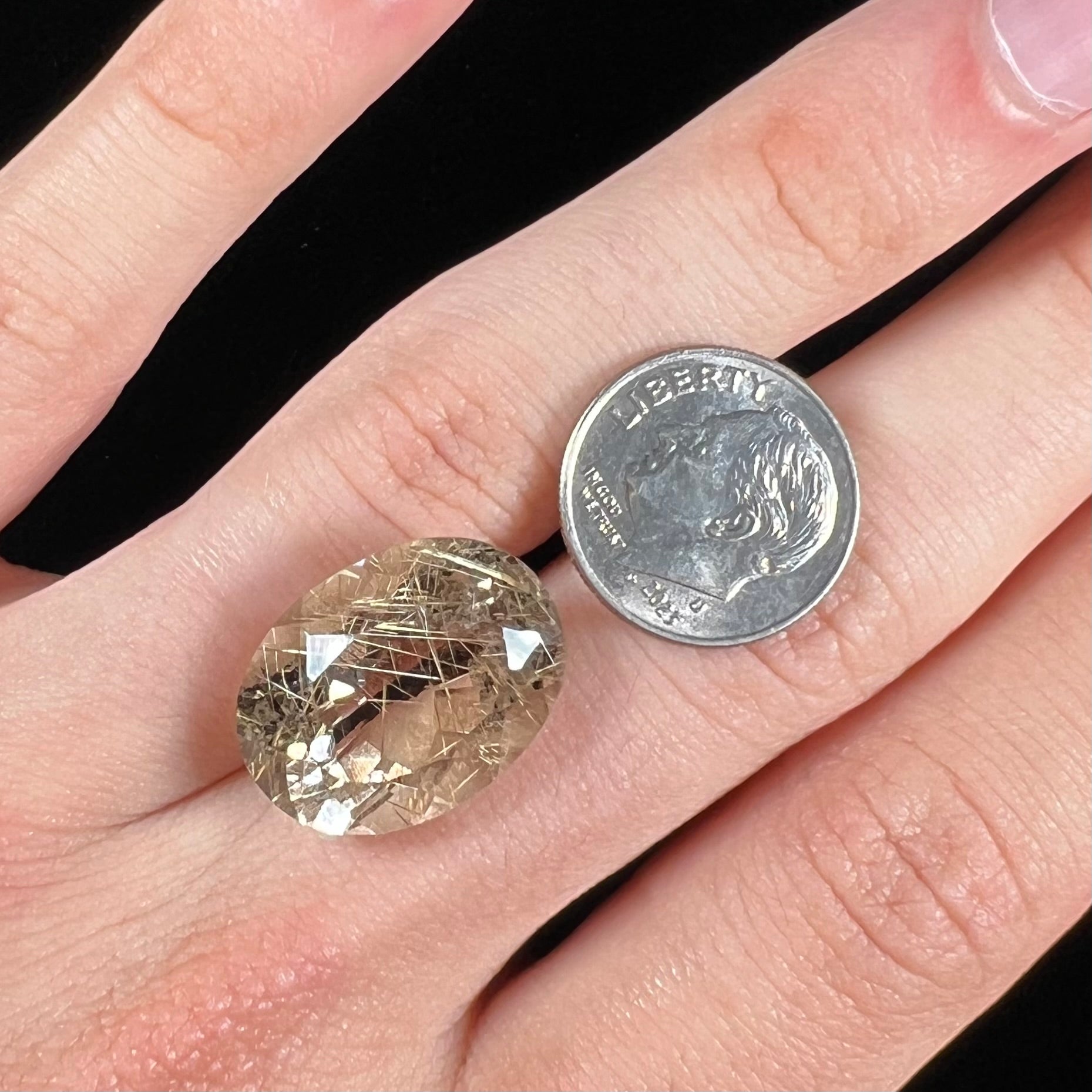 A faceted oval cut rutilated quartz gemstone.  The stone is smoky color with golden rutile needle inclusions.