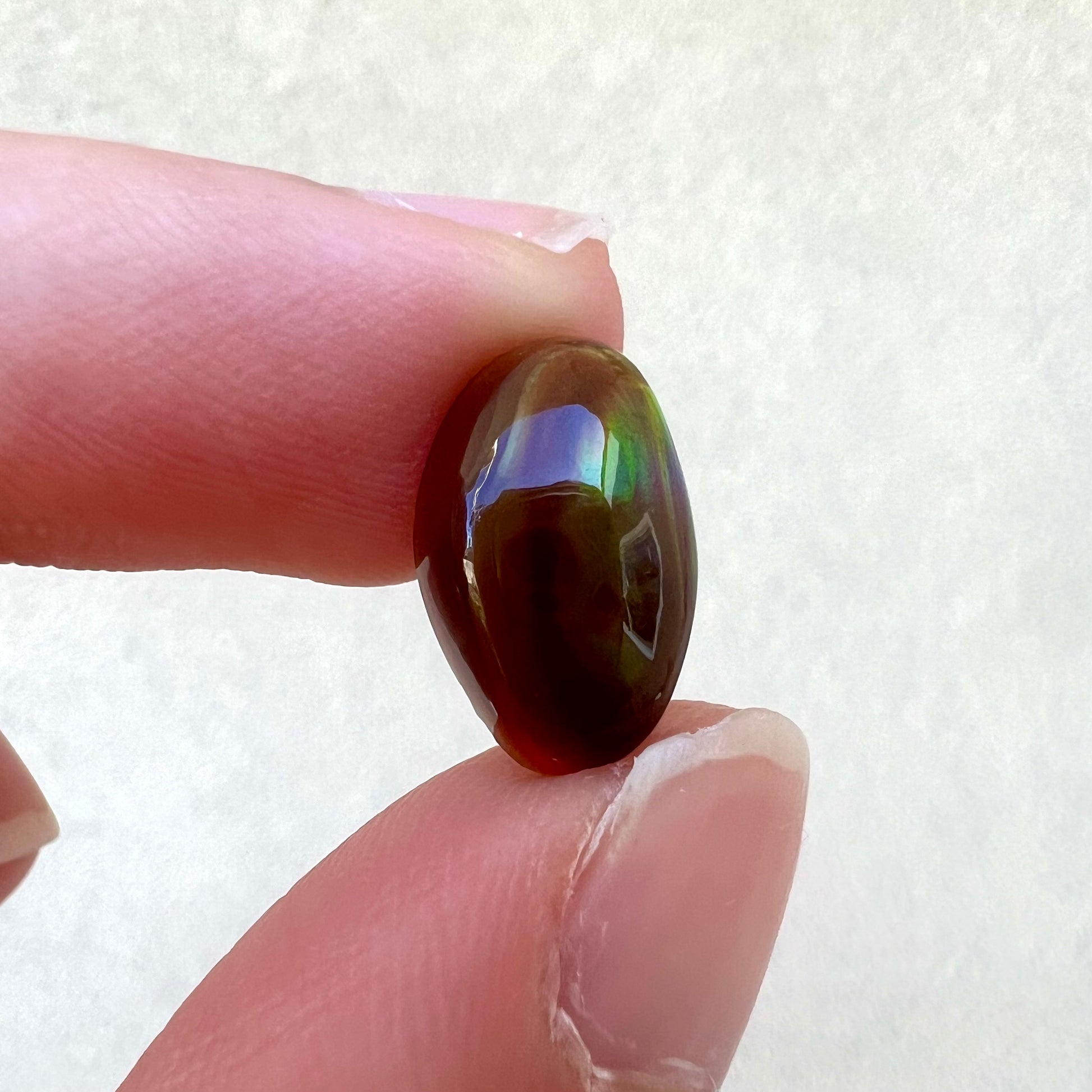 A loose, oval cabochon cut fire agate stone that shines red, yellow, green, blue, and purple.