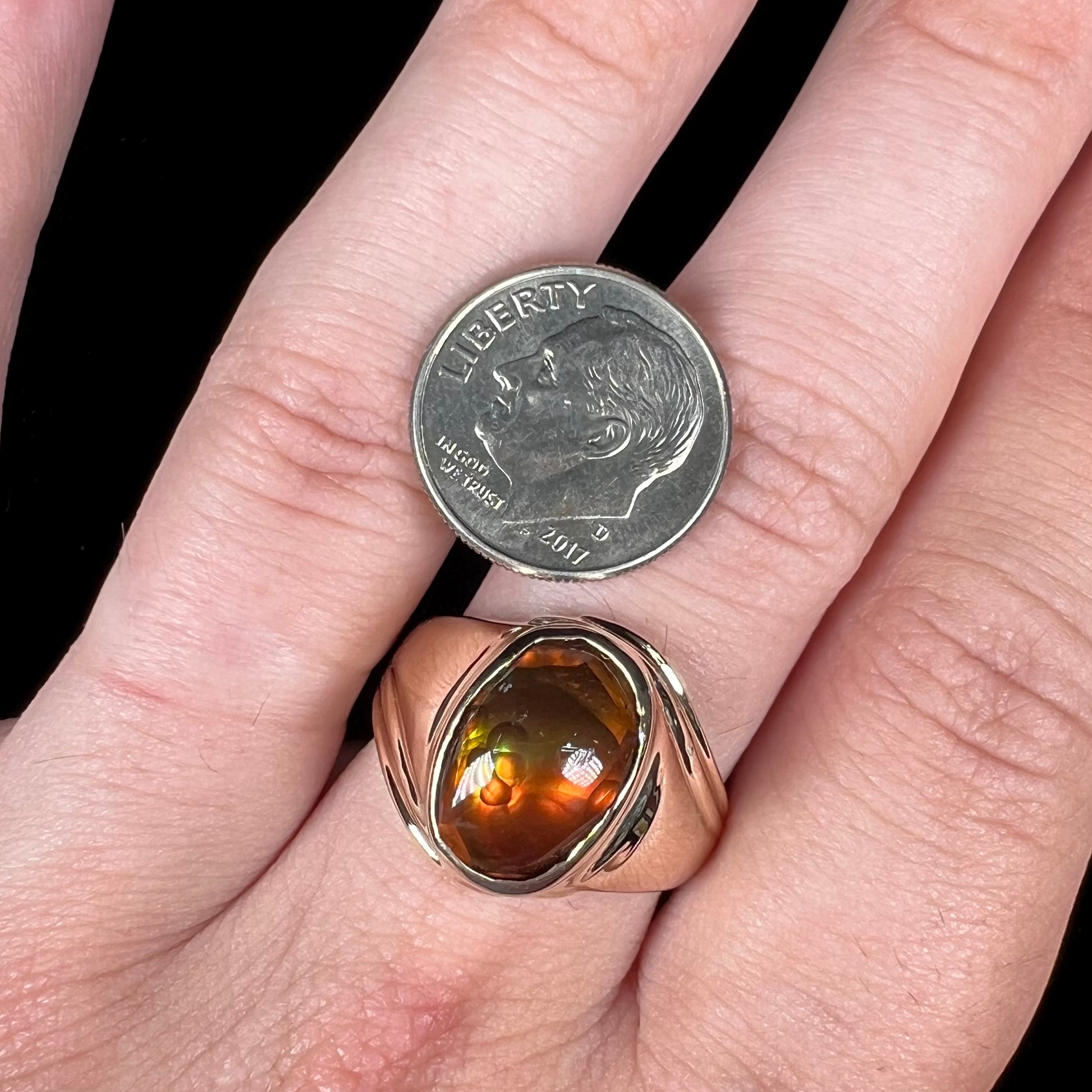 A men's yellow gold solitaire ring set with an oval cabochon cut fire agate stone.  The stone is red and green.