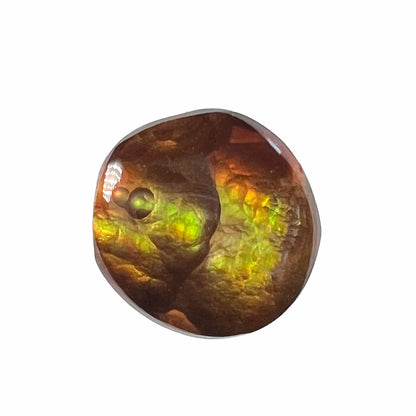 A loose, round cabochon cut fire agate stone.  The gem is green with orange, red, blue, and a purple stripe.
