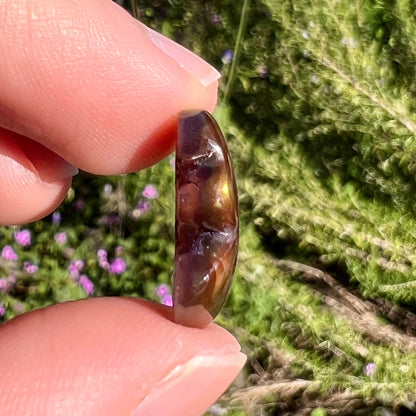 A polished, freeform shaped fire agate stone.  The stone is purple, green, and blue with red and yellow banding.