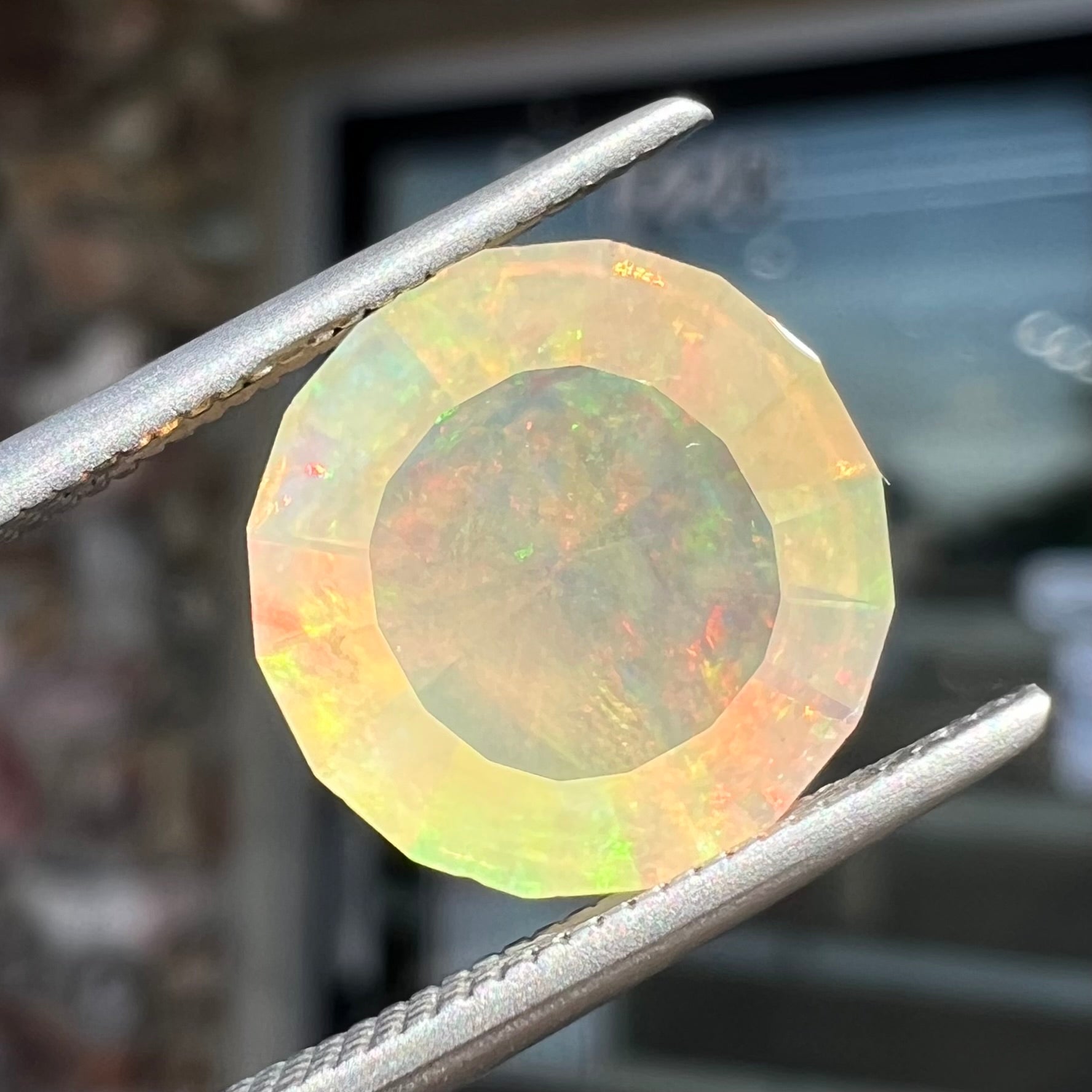 A loose, round faceted Mexican fire opal gemstone.  The stone is transluscent light orange color with rainbow play of color in the sunlight.