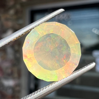 A loose, round faceted Mexican fire opal gemstone.  The stone is transluscent light orange color with rainbow play of color in the sunlight.