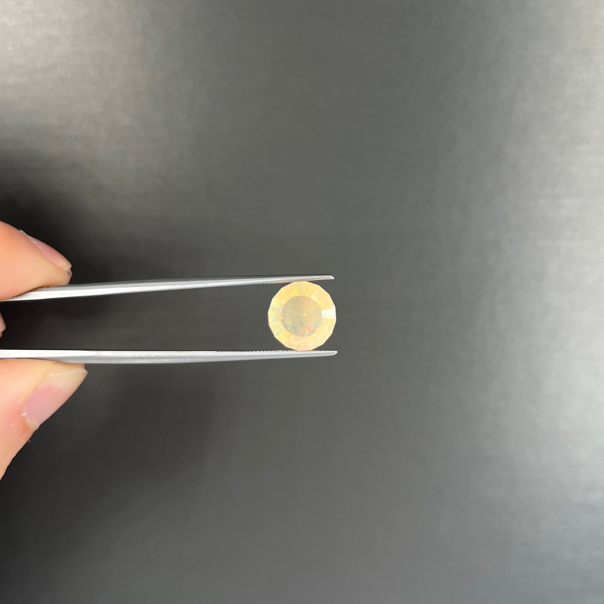A loose, round faceted Mexican fire opal gemstone.  The stone is transluscent light orange color with rainbow play of color in the sunlight.