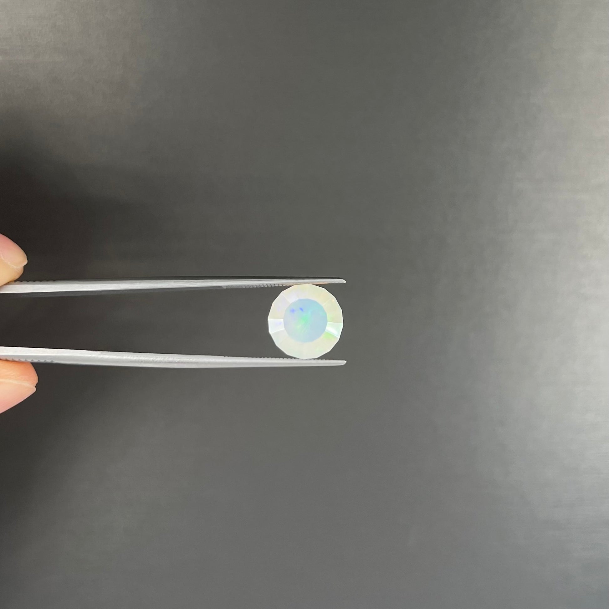 A loose, modified round cut Mexican fire opal gemstone.  The stone is transluscent light yellow with green and blue fire.