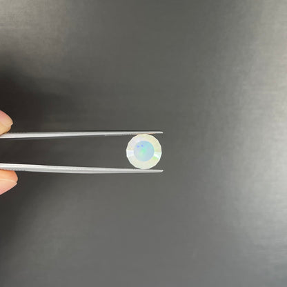 A loose, modified round cut Mexican fire opal gemstone.  The stone is transluscent light yellow with green and blue fire.