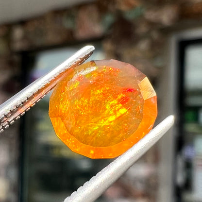 A loose, round faceted cut fire opal from Mexico.  The body color is yellowish orange with red, green, and yellow fire.