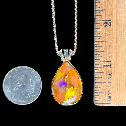 A unisex pear shaped fire opal pendant set with tapered baguette cut diamond accents in 18 karat gold.