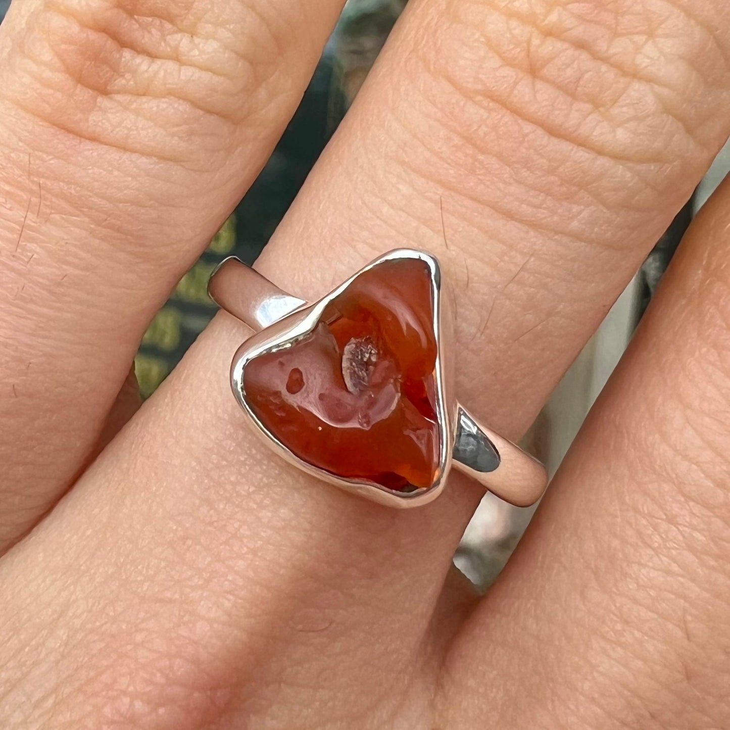 A polished fire opal crystal bezel set into a sterling silver ring.  The opal is an orange color.
