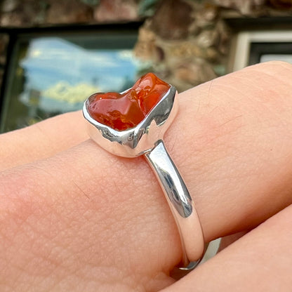 A polished fire opal crystal bezel set into a sterling silver ring.  The opal is an orange color.