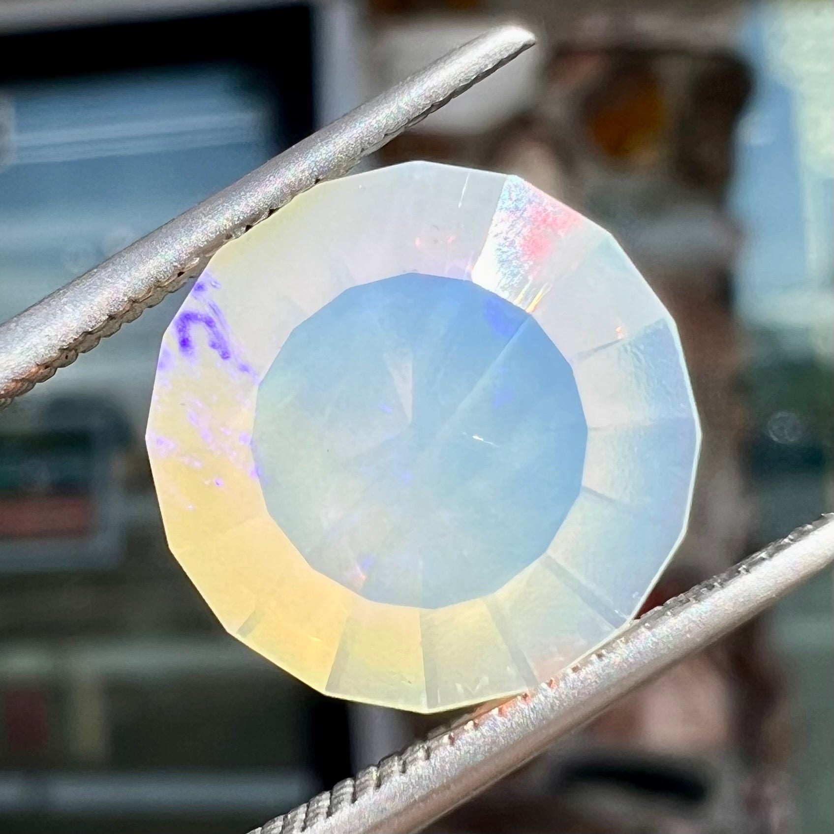 A loose, modified round cut Mexican fire opal gemstone.  The stone is transluscent light yellow with green and blue fire.
