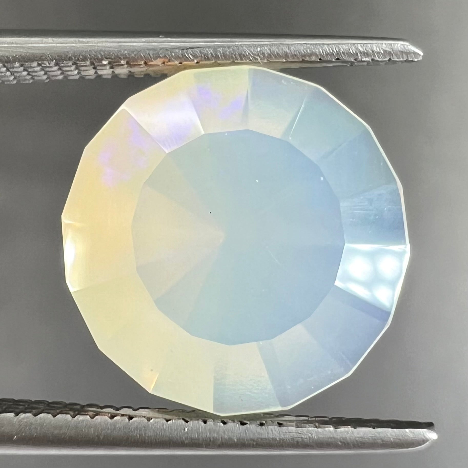 A loose, modified round cut Mexican fire opal gemstone.  The stone is transluscent light yellow with green and blue fire.