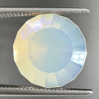 A loose, modified round cut Mexican fire opal gemstone.  The stone is transluscent light yellow with green and blue fire.