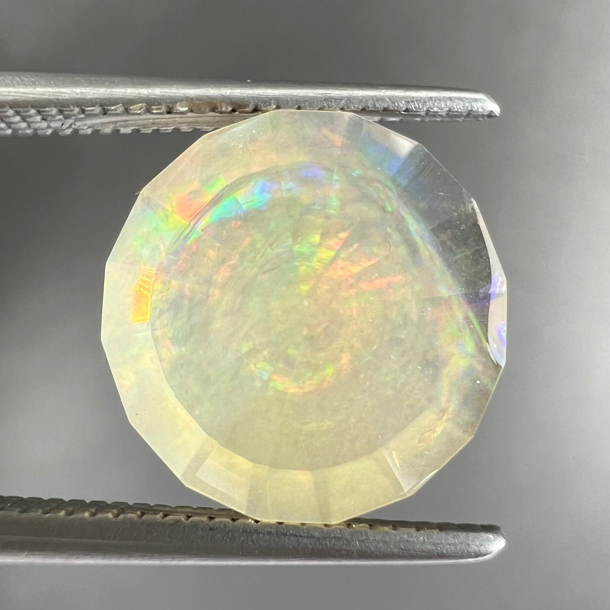 A loose, round faceted Mexican fire opal gemstone.  The stone is transluscent light orange color with rainbow play of color in the sunlight.
