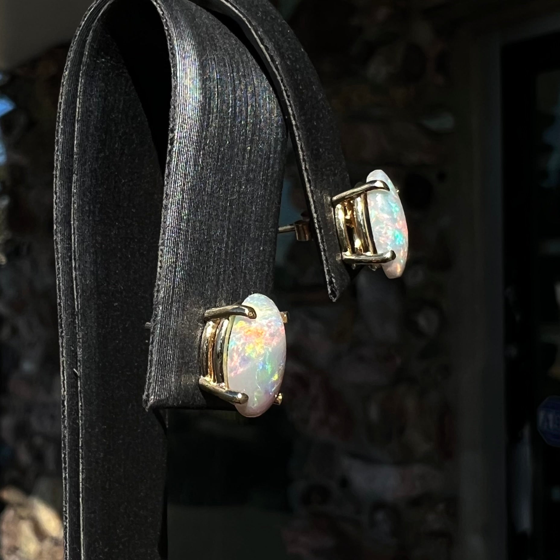 A pair of natural, semi-black crystal opal stud earrings in yellow gold.  The opals are oval cabochon cut.