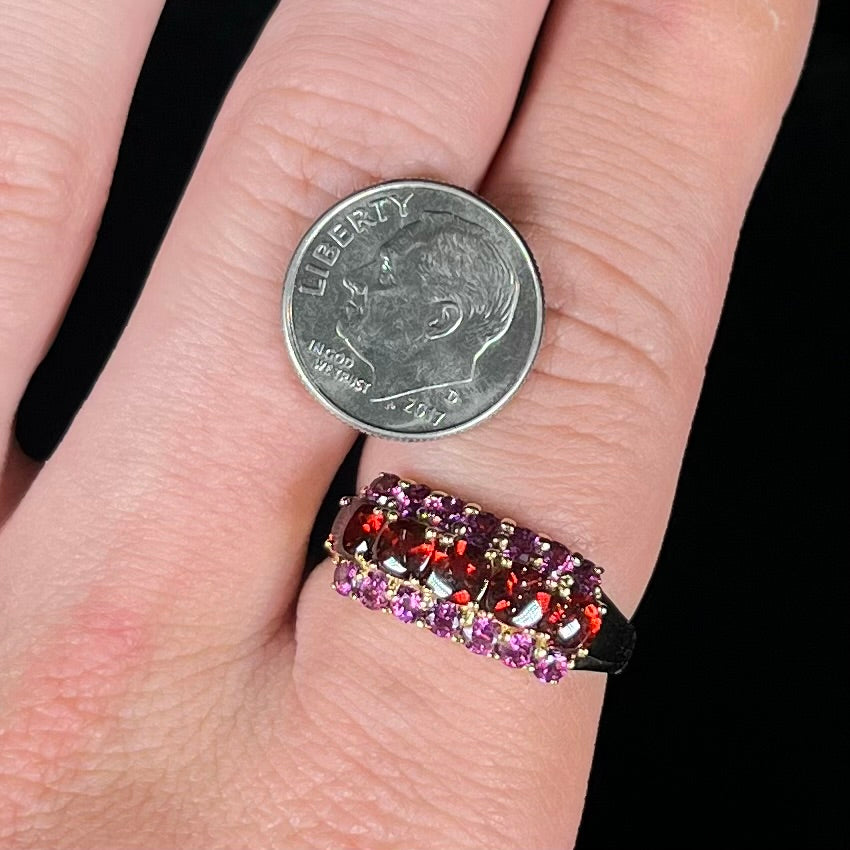 A gold ring set with buff cut cushion shaped almandine garnets with round cut purple rhodolite garnet accents.