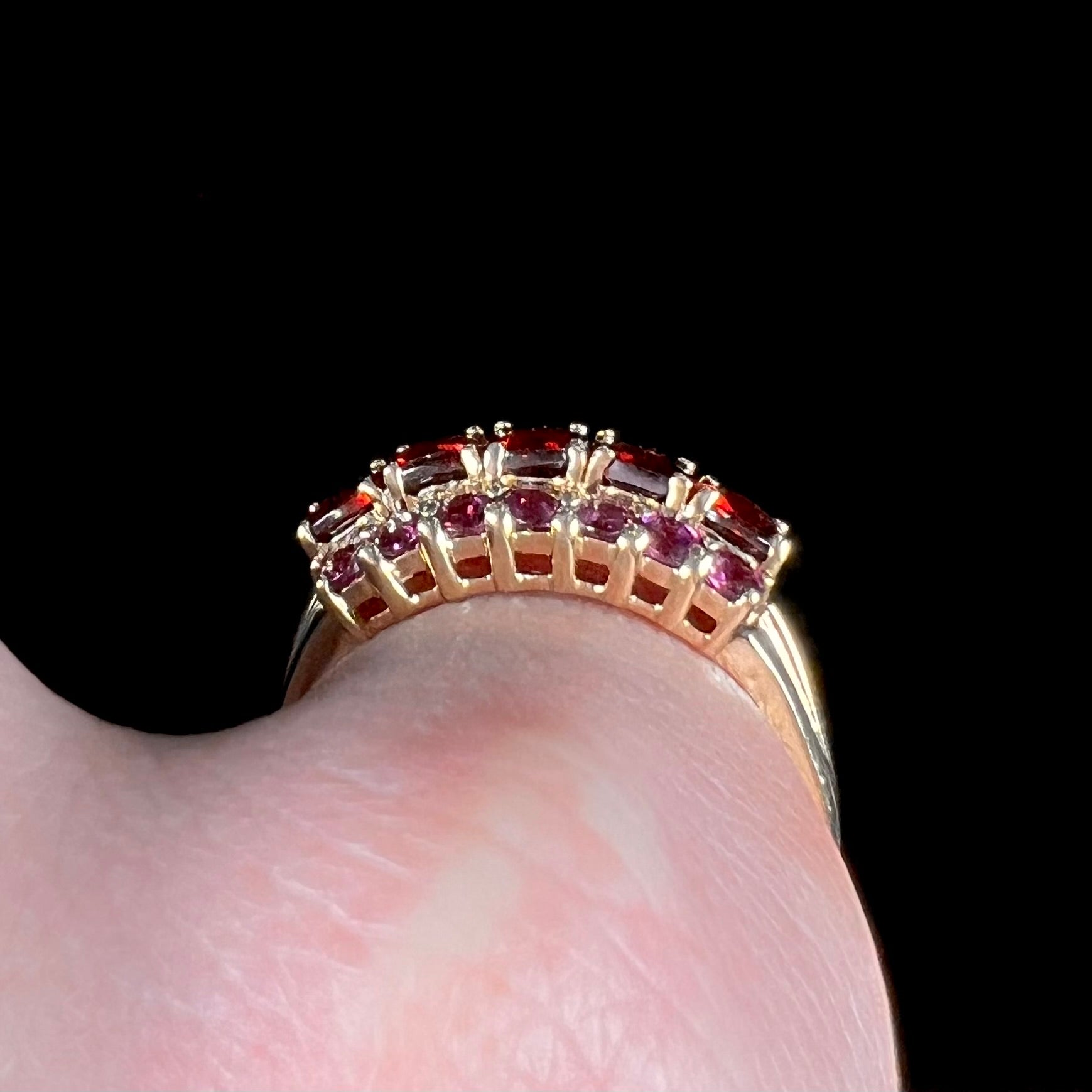 A gold ring set with buff cut cushion shaped almandine garnets with round cut purple rhodolite garnet accents.