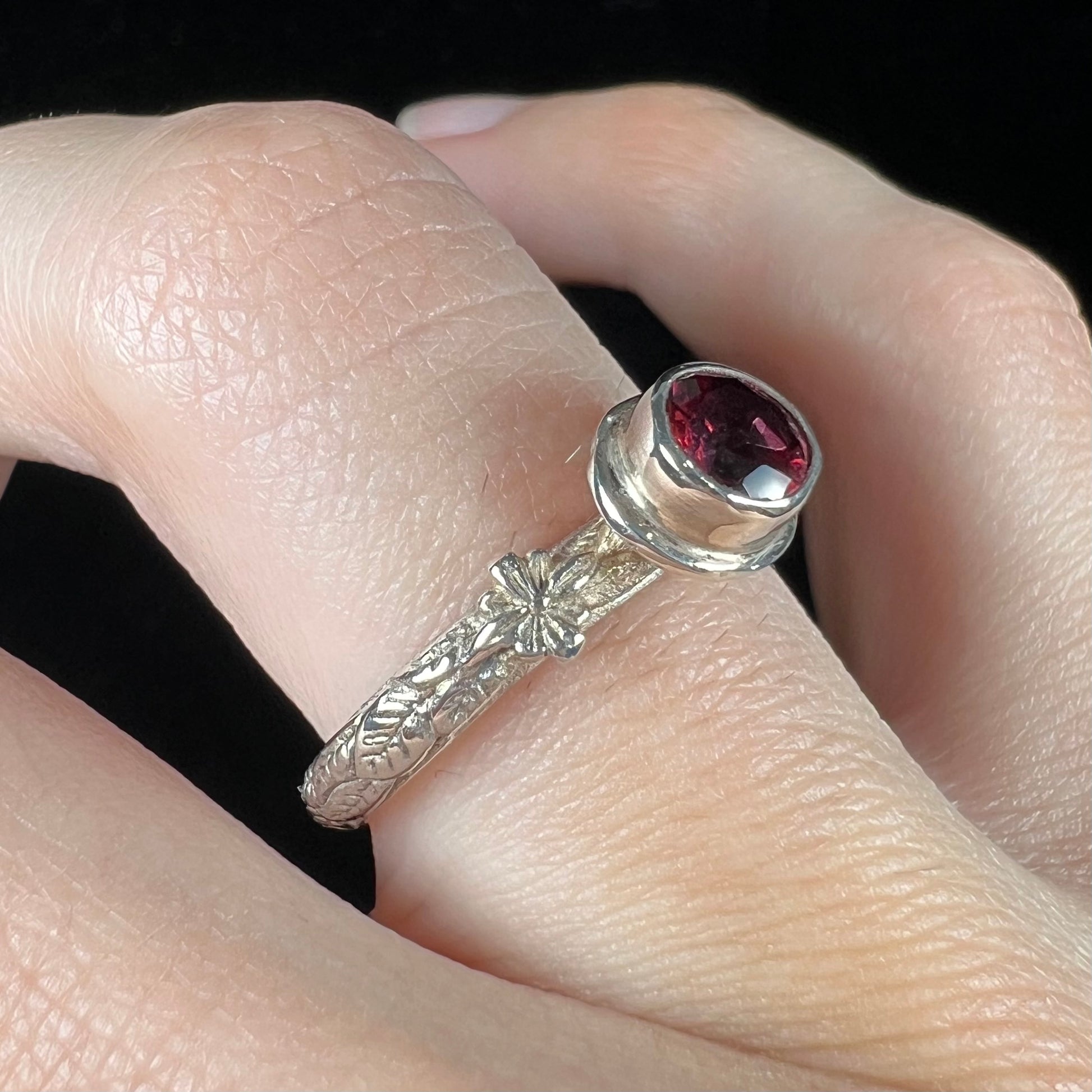 A ladies' sterling silver purple rhodonite garnet solitaire ring.  The shank has an etched floral leaf design.