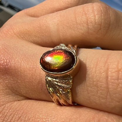 A unisex oval cabochon cut fire agate ring cast in yellow gold.  The stone flashes green and red colors.