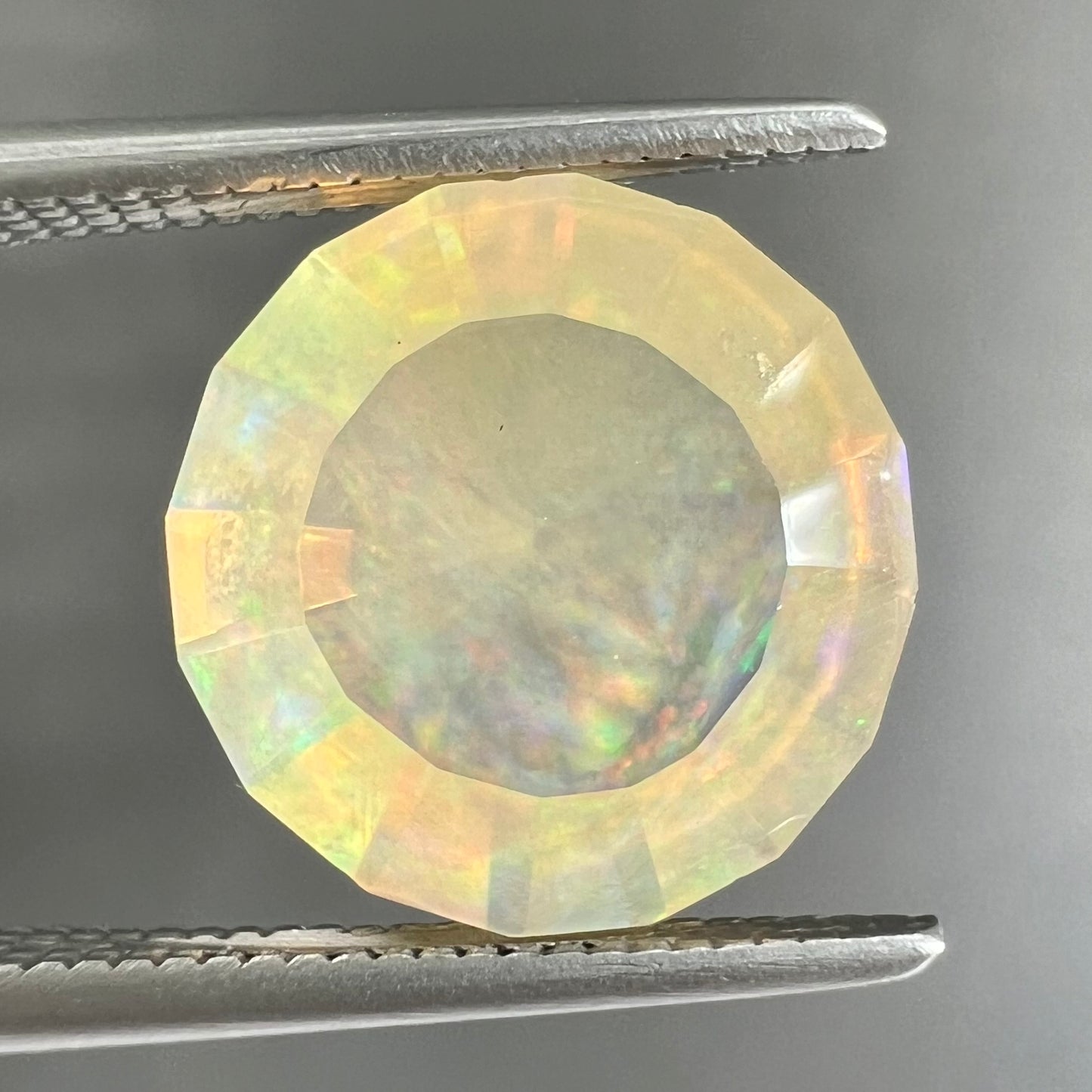 A loose, round faceted Mexican fire opal gemstone.  The stone is transluscent light orange color with rainbow play of color in the sunlight.