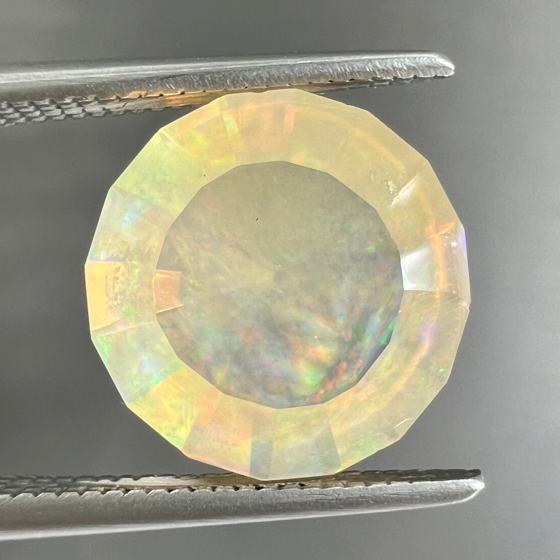 A loose, round faceted Mexican fire opal gemstone.  The stone is transluscent light orange color with rainbow play of color in the sunlight.