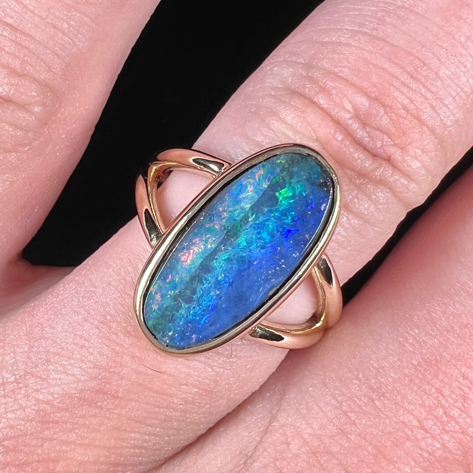 A ladies' yellow gold split shank solitaire ring set with a natural Australian black boulder opal.