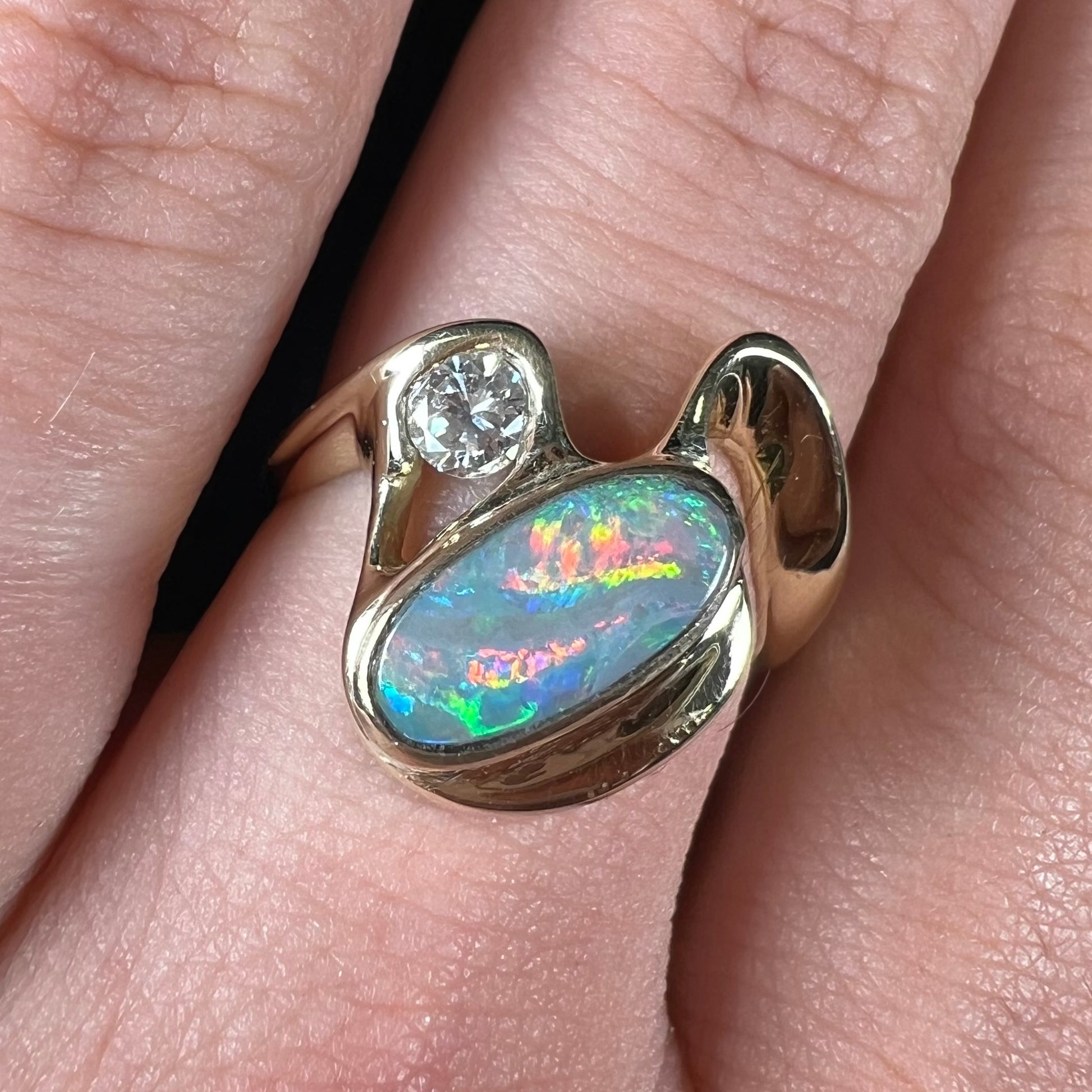 A ladies' yellow gold, bezel set ring mounted with a natural 1.15 carat black opal and round diamond.