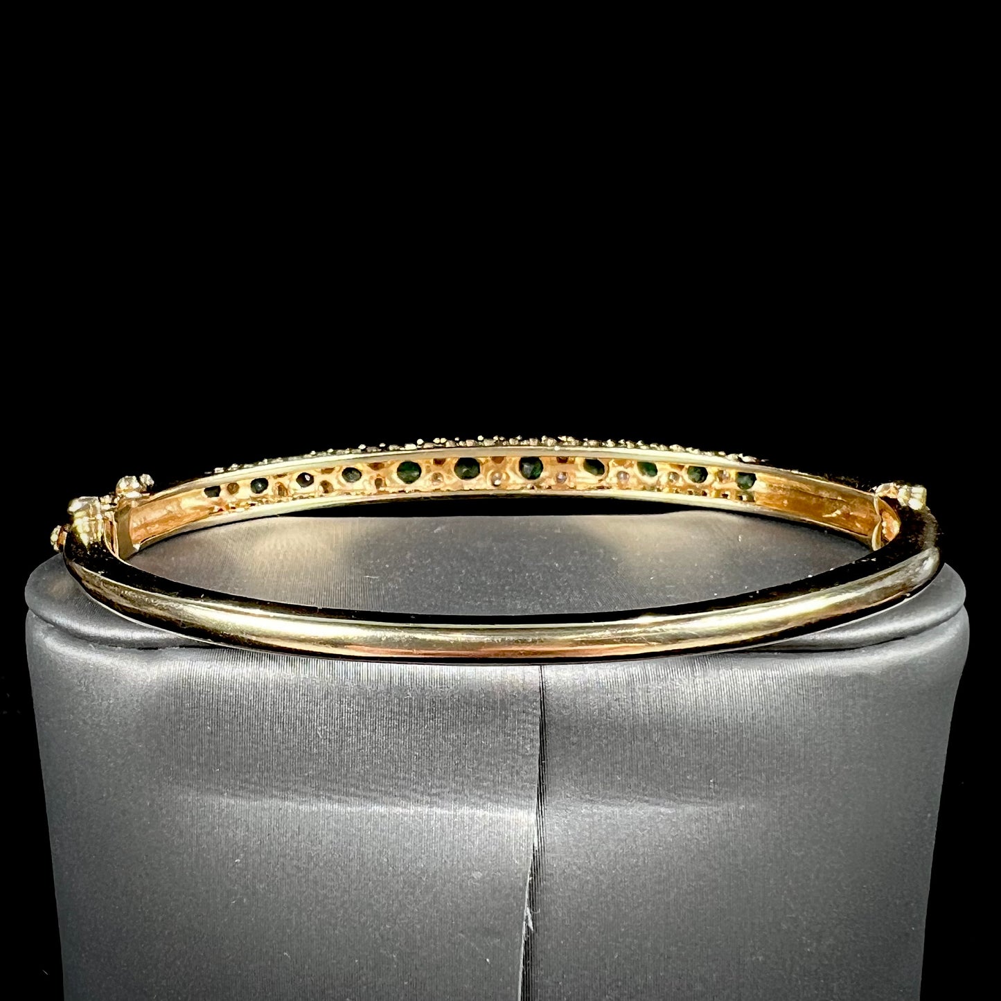 A ladies' yellow gold bangle bracelet set with round cut emeralds and diamonds.