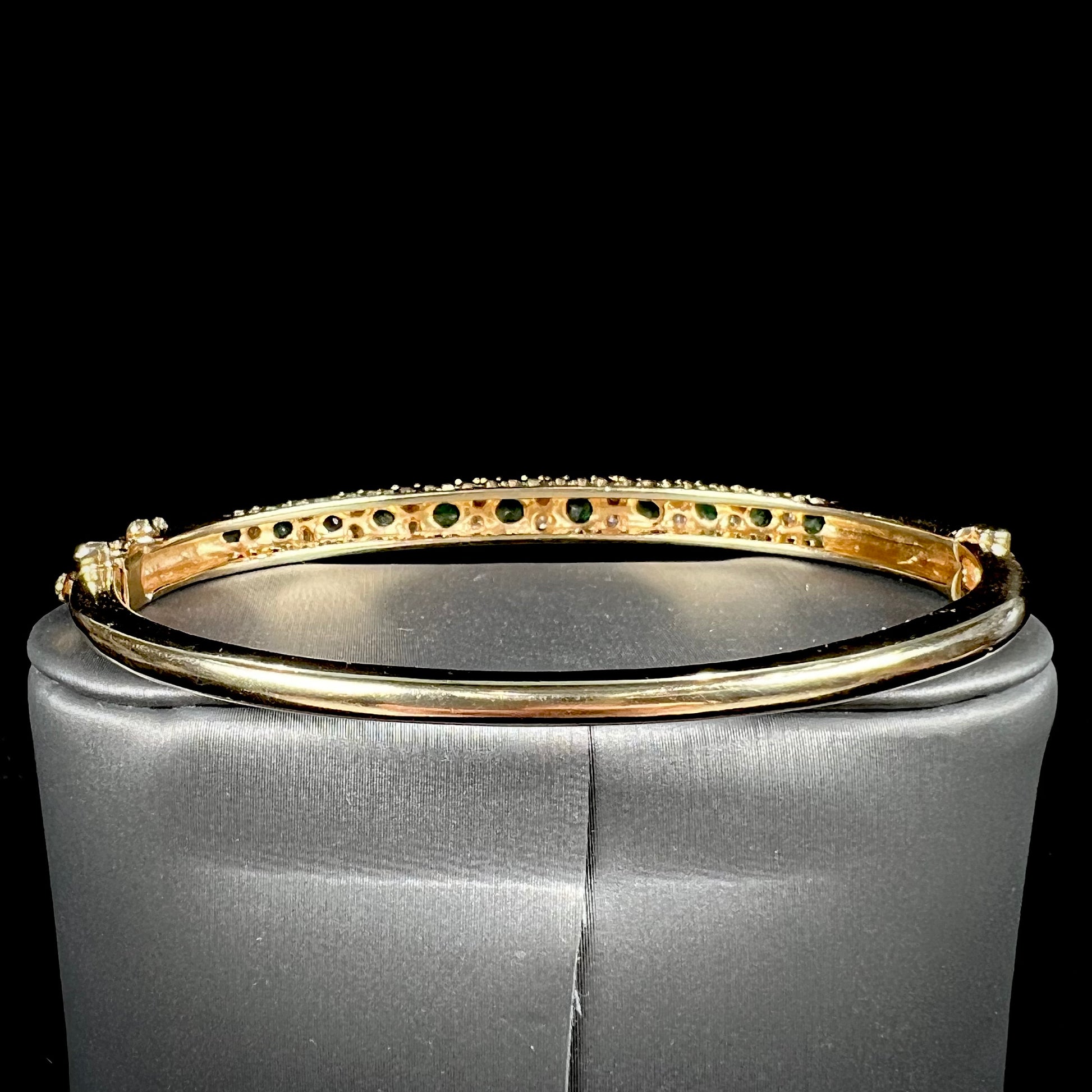 A ladies' yellow gold bangle bracelet set with round cut emeralds and diamonds.
