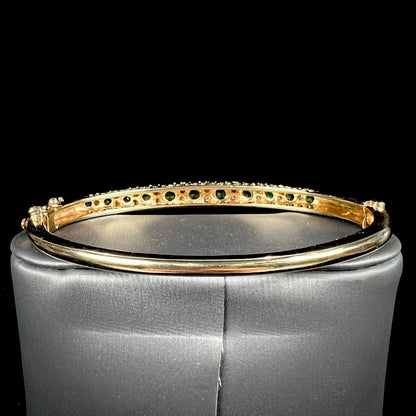 A ladies' yellow gold bangle bracelet set with round cut emeralds and diamonds.