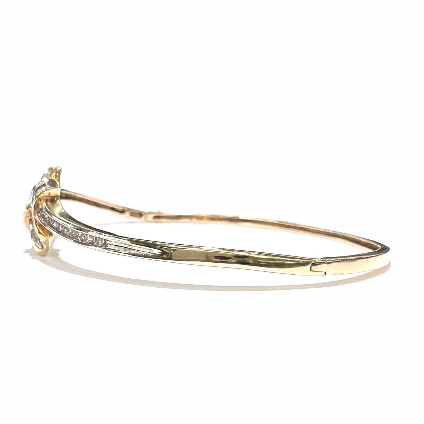 A ladies' knot style yellow gold bangle bracelet set with round and baguette cut diamonds.