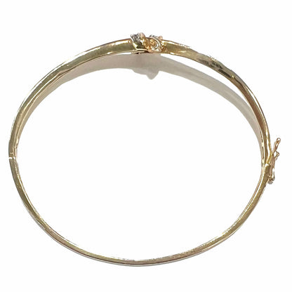 A ladies' knot style yellow gold bangle bracelet set with round and baguette cut diamonds.