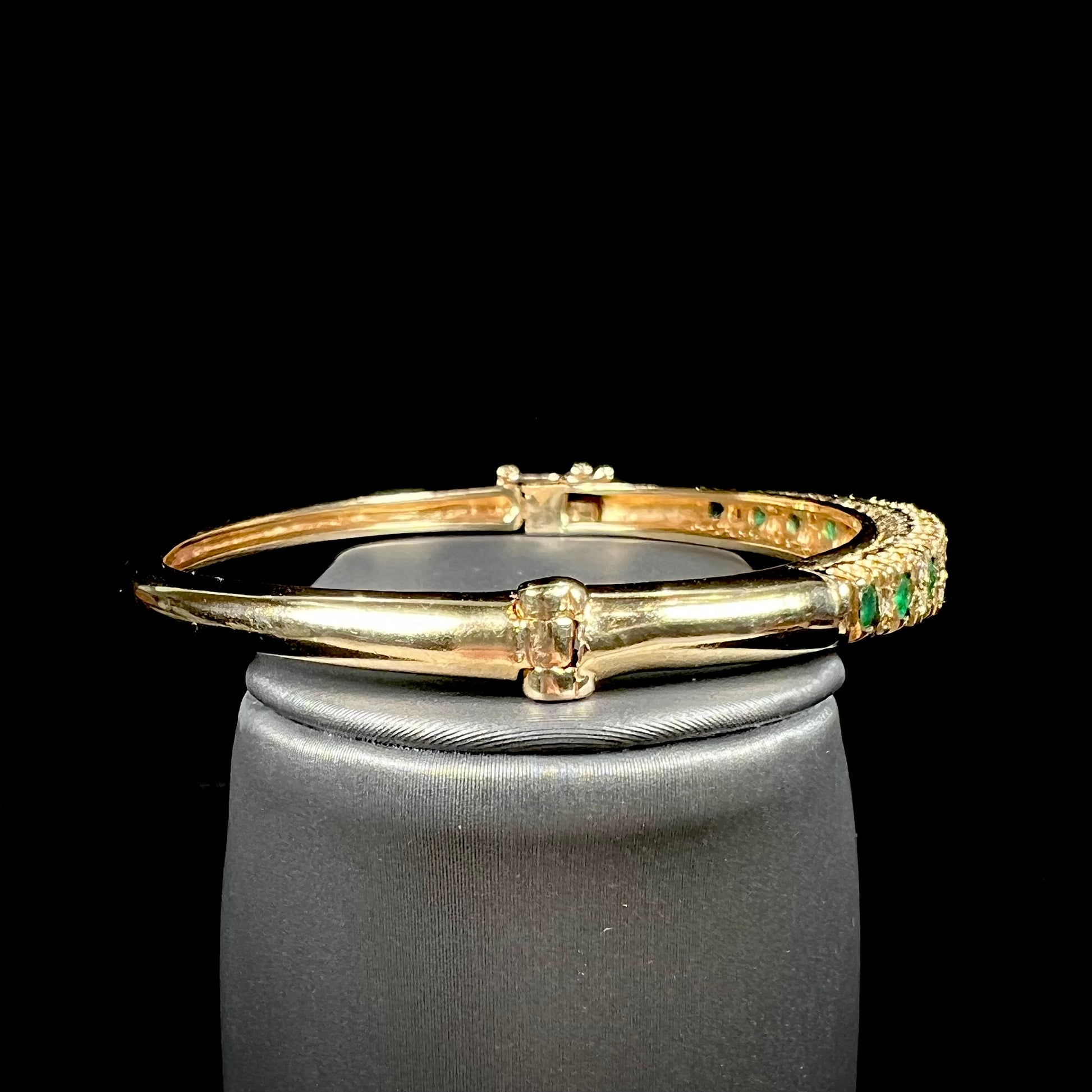 A ladies' yellow gold bangle bracelet set with round cut emeralds and diamonds.