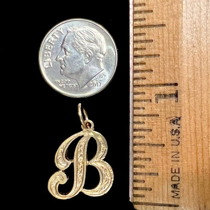 A 14 karat yellow gold stylized script letter "B" pendant, resembling the Barbie logo.