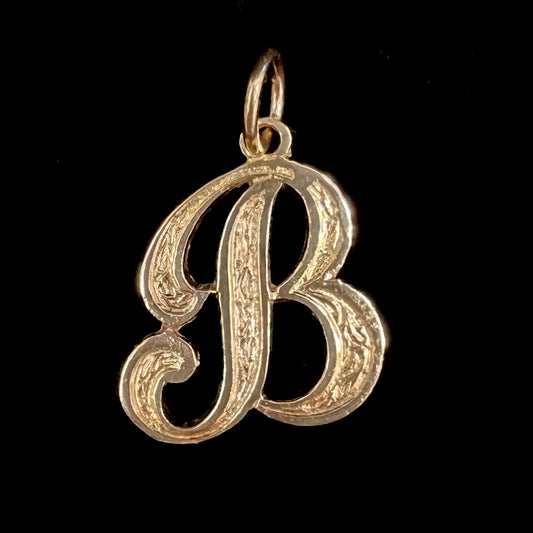 A 14 karat yellow gold stylized script letter "B" pendant, resembling the Barbie logo.