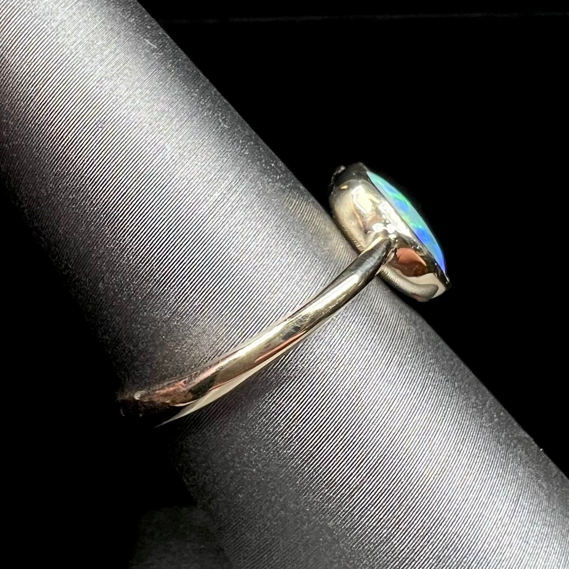 A ladies' oval cut black crystal opal solitaire ring handmade with a single split shank in yellow gold.