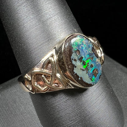 A unisex Celtic style natural boulder opal ring cast in yellow gold.  The opal shines green and blue.