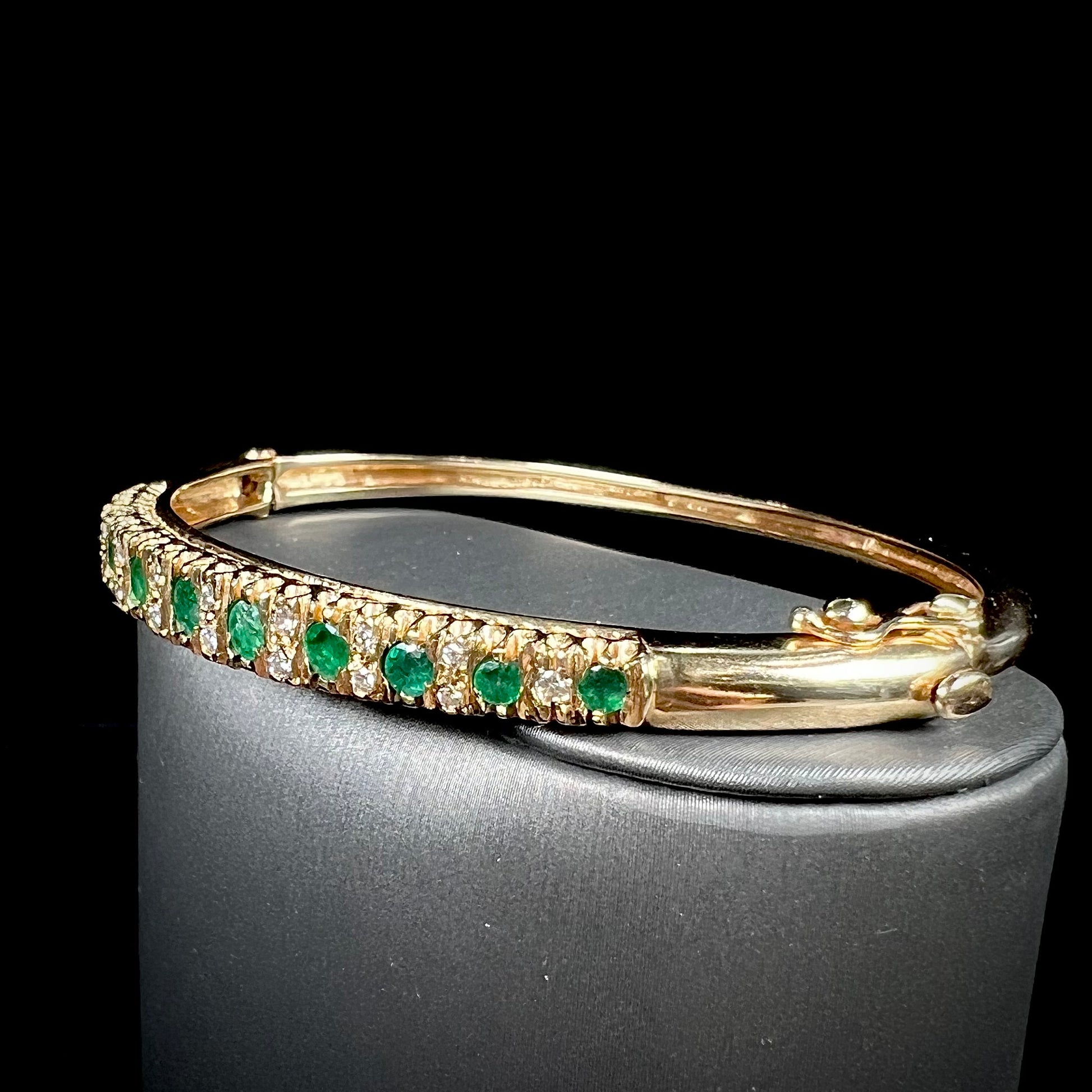 A ladies' yellow gold bangle bracelet set with round cut emeralds and diamonds.