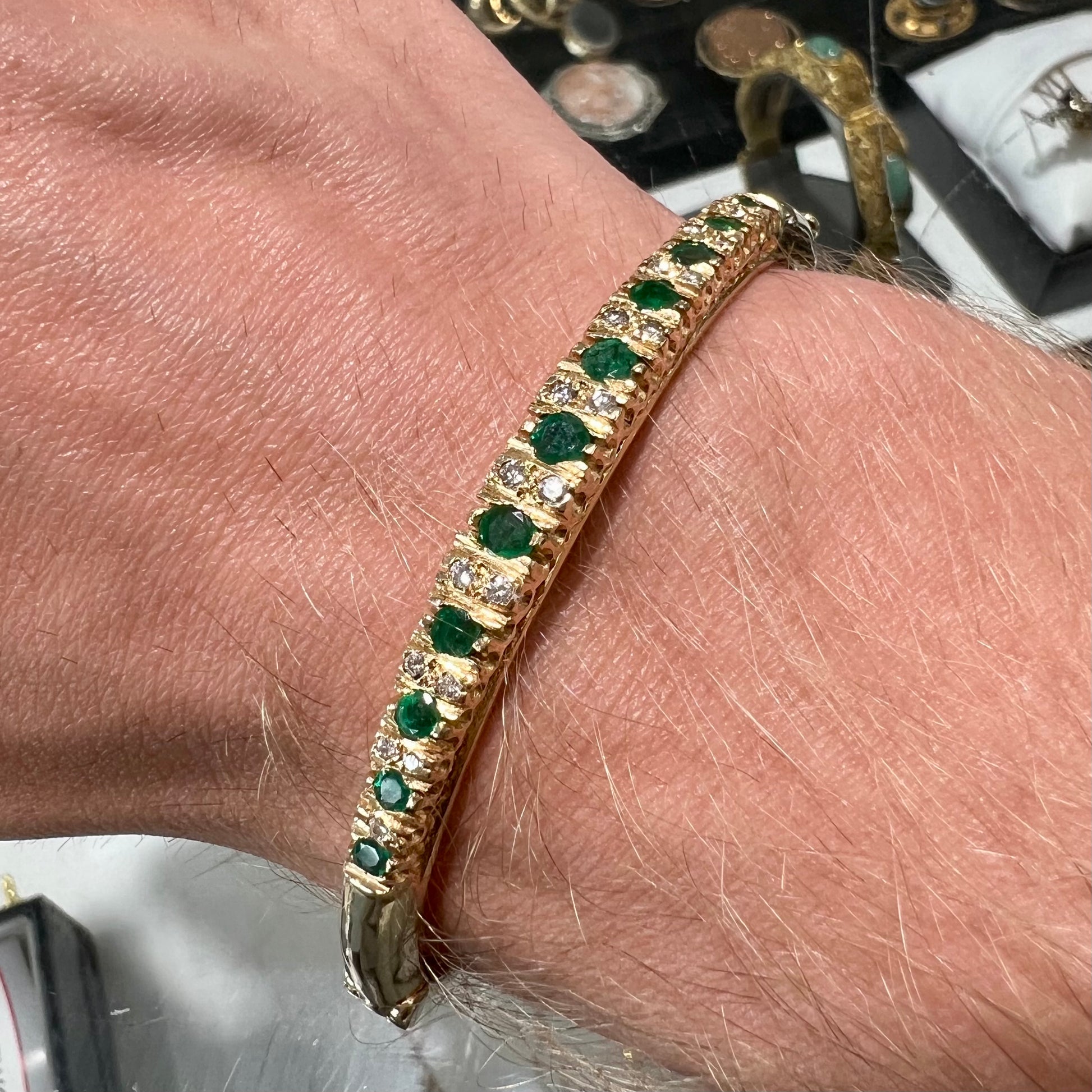 A ladies' yellow gold bangle bracelet set with round cut emeralds and diamonds.