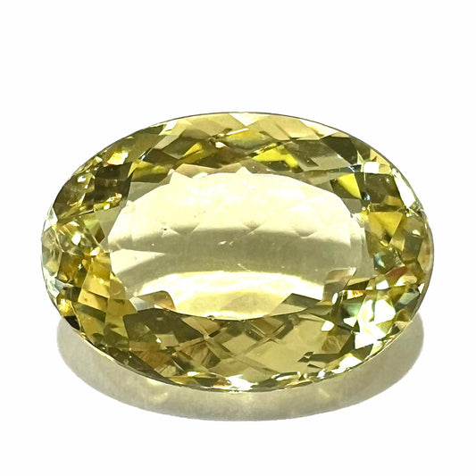A faceted oval cut golden beryl gemstone.  The stone is a greenish light yellow.
