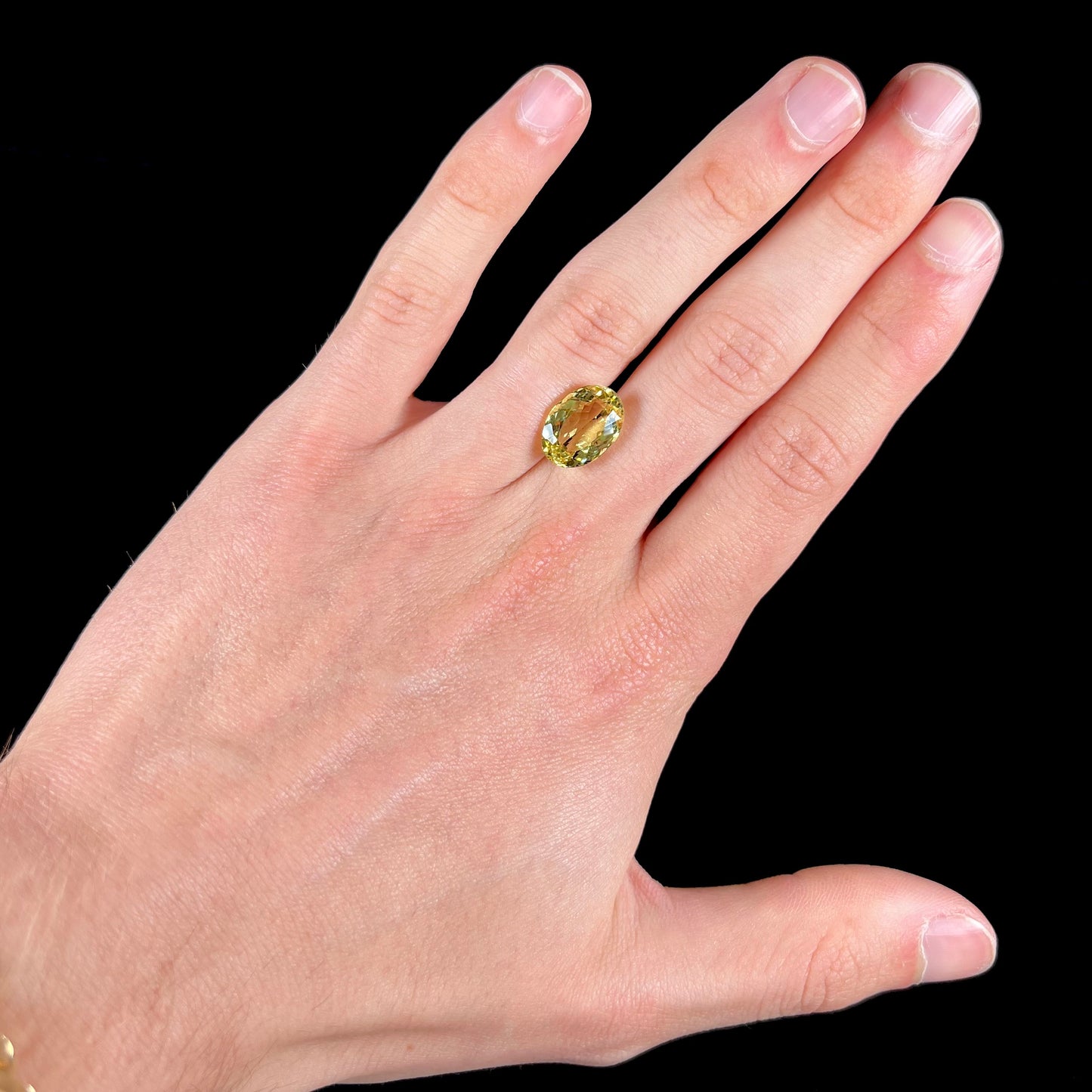 A faceted oval cut golden beryl gemstone.  The stone is a greenish light yellow.