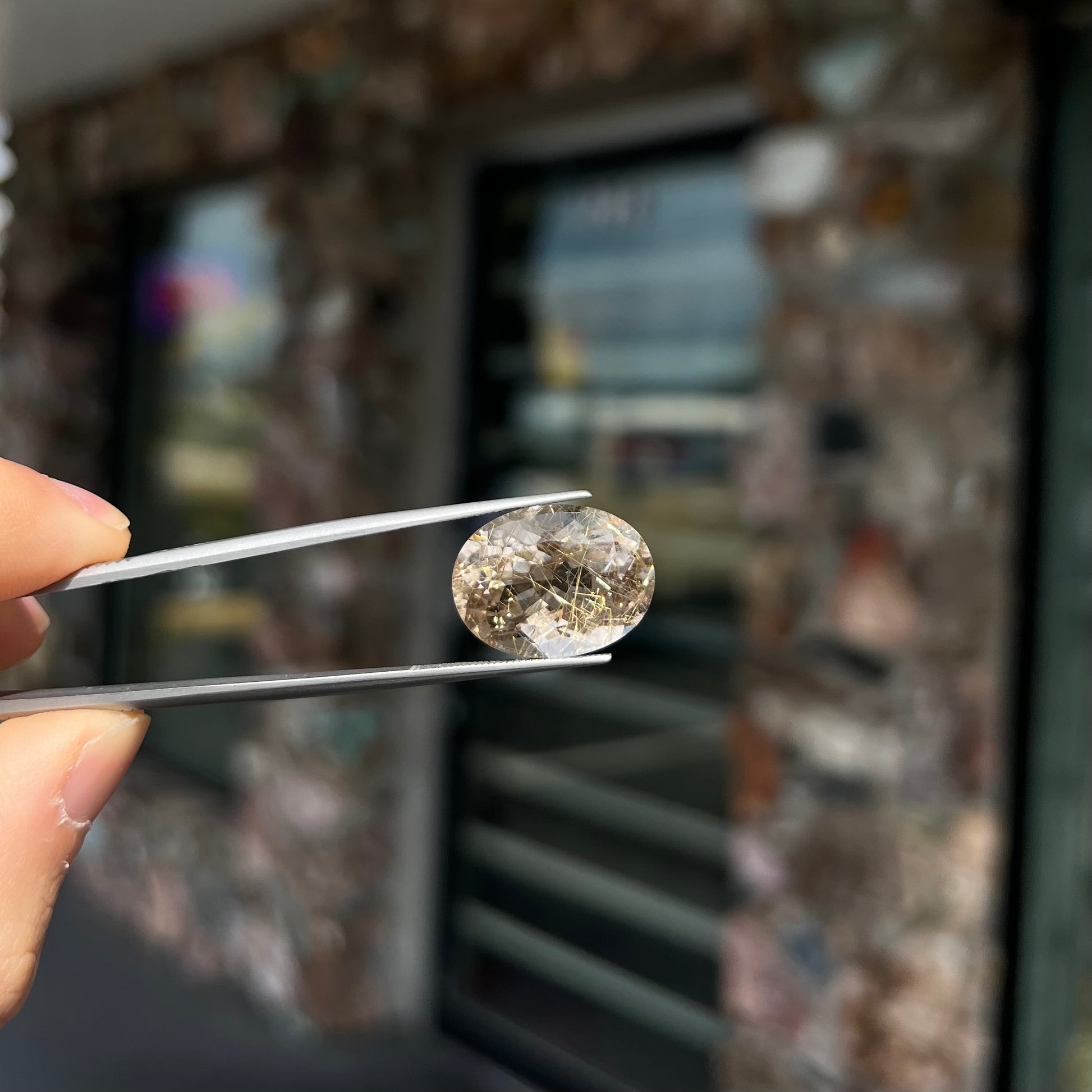 A faceted oval cut rutilated quartz gemstone.  The stone is smoky color with golden rutile needle inclusions.