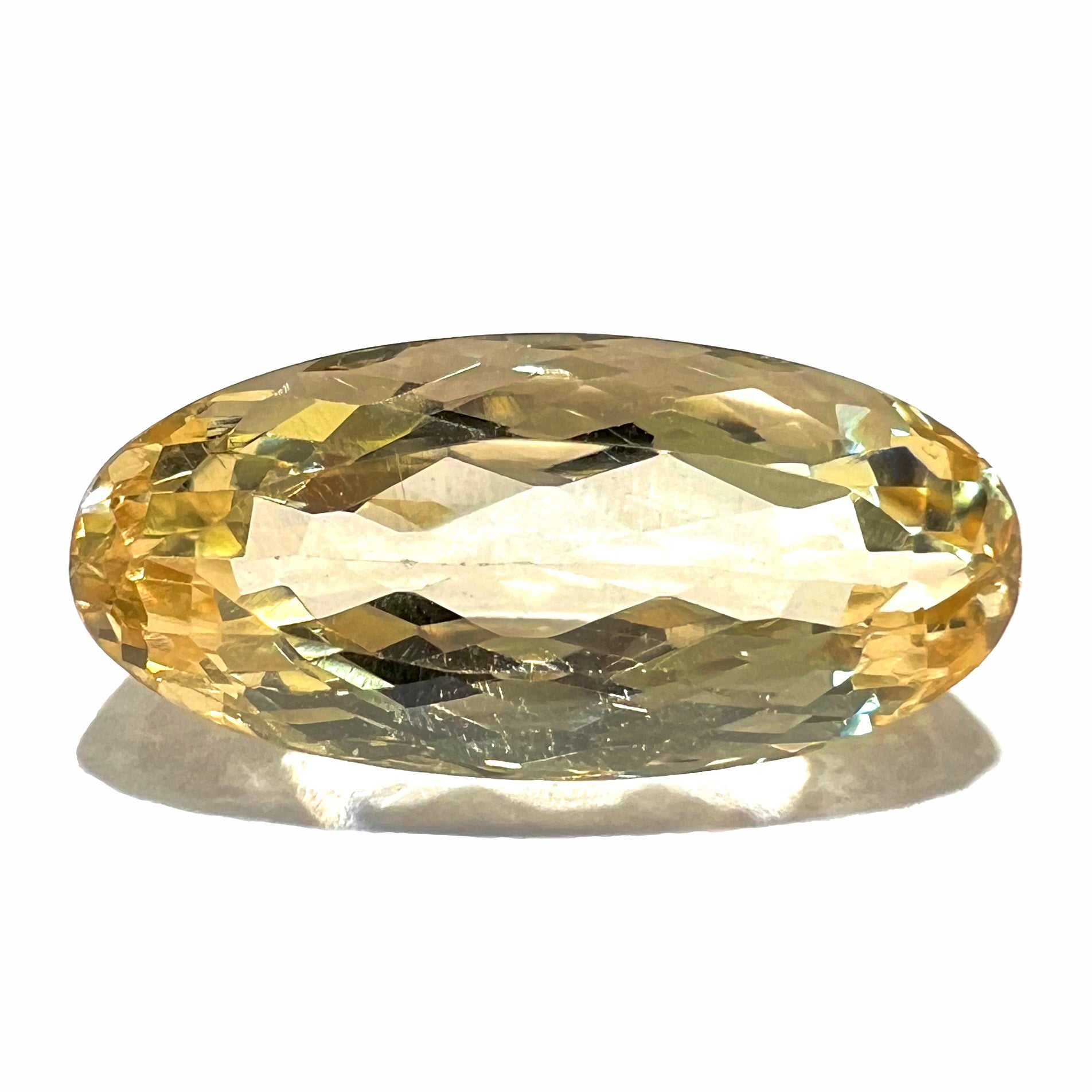 A loose, oval cut golden topaz gemstone.  A stronger concentration of yellow rests in the edges of the stone.