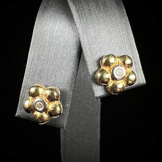 A pair of two-tone yellow and white gold diamond flower earrings.  The flower petals are yellow gold, and the diamonds are set in white gold bezels.