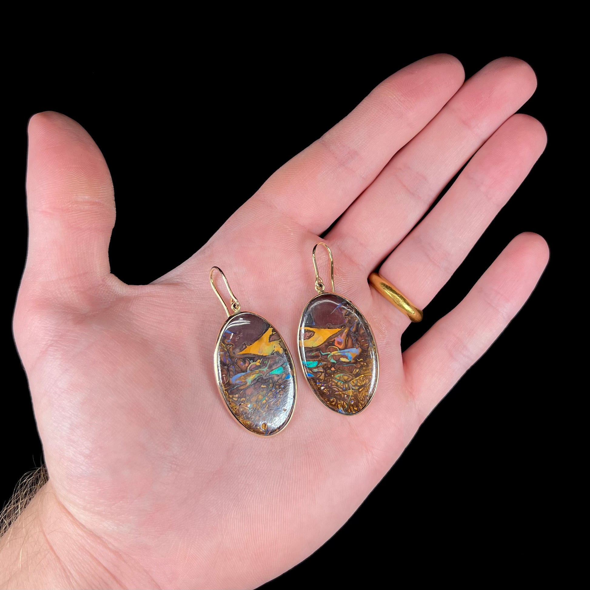 A pair of oval cut Koroit boulder opal dangle earrings in yellow gold bezel frames.  The opal exhibits a unique pattern and blue colors.