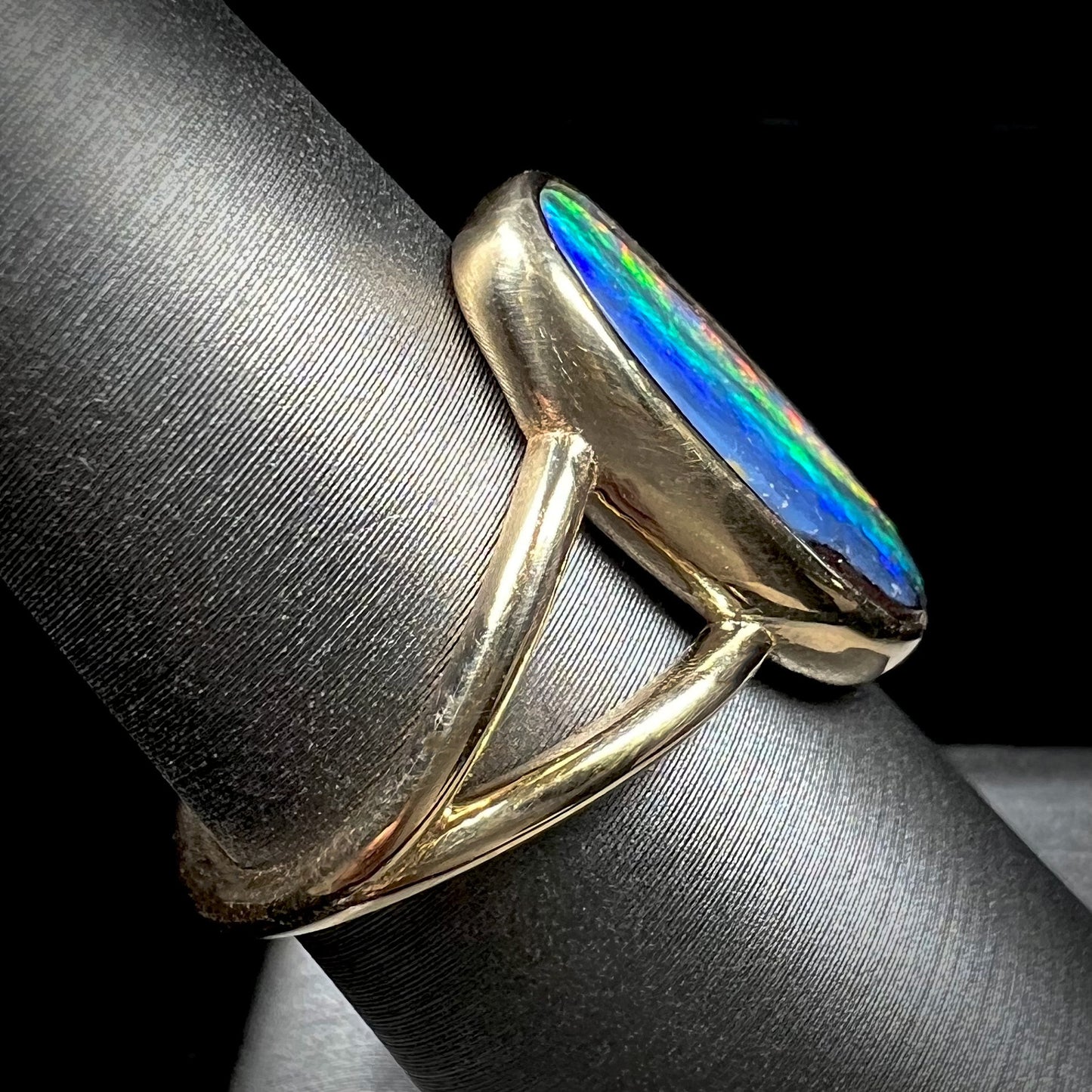 A ladies' yellow gold split shank solitaire ring set with a natural Australian black boulder opal.
